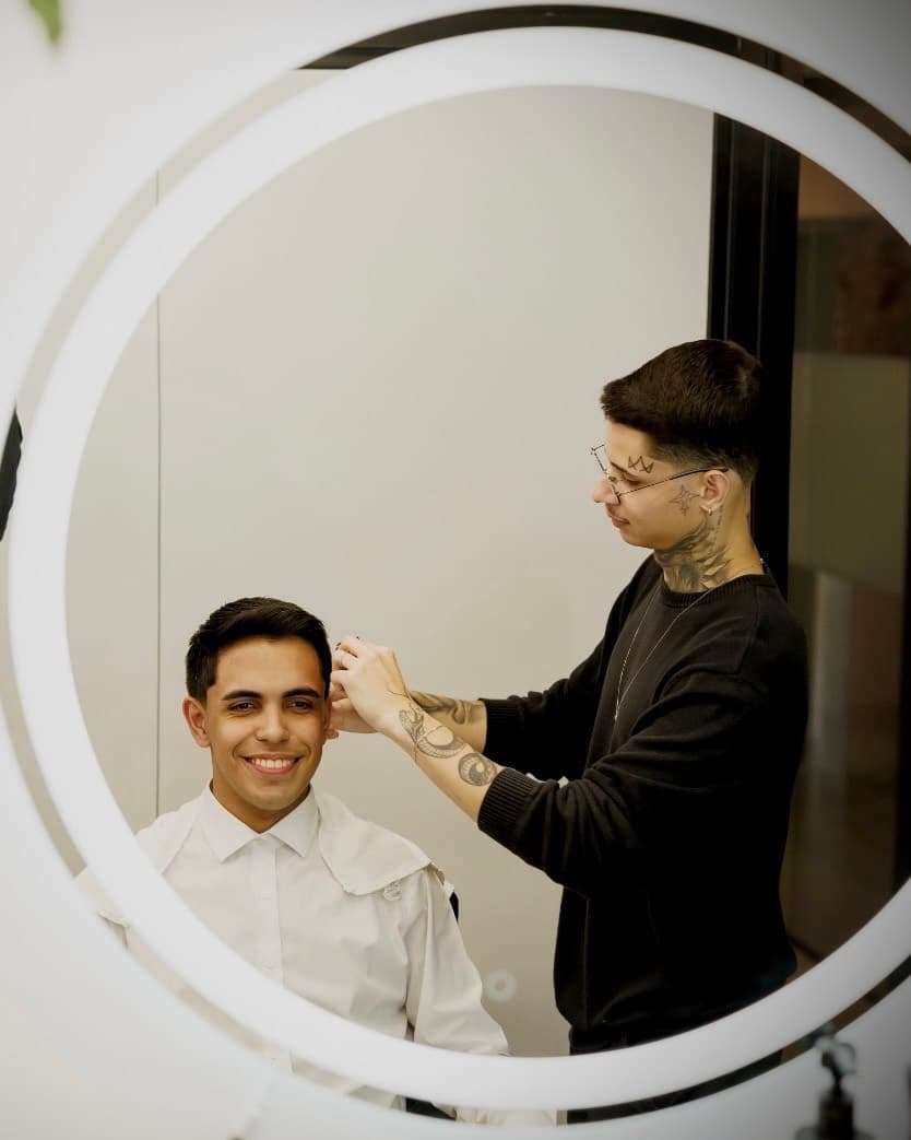 Gustavo Derussi ajustando o corte de um cliente diante do espelho da barbearia, em Joinville